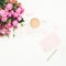 Female desk with pink roses bouquet, pink diary, coffee mug and marshmallows on white background. Flat lay. Top view feminine back