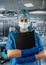 Female doctor in blue uniform and protective mask, gloves writes notes on the clipboard in operating room