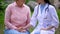 Female doctor comforting aged patient sitting hospital garden, clinic service