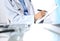 Female doctor filling up medical form on clipboard, closeup. Reflecting glass table is a physician working place