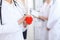 Female doctor holding heart in her hands. Doctor and patient sitting in the background. Cardiology in medicine an