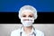 Female doctor in medical mask with the inscription COVID-19 on a blurred background of the flag of Estonia. Pandemic virus COVID-