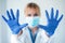 Female doctor with a medical mask showing hands to camera while wearing a blue nitrile gloves over white background