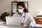 Female doctor in medical uniform and facemask work on laptop