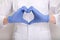 A female doctor or nurse in blue protective gloves making heart shape symbol with hands, therapy, treatment and insurance concept