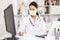 Female doctor in in protective medical mask working on laptop