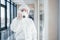 Female doctor scientist in lab coat, defensive eyewear and mask standing indoors with antibacterial spray