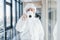 Female doctor scientist in lab coat, defensive eyewear and mask standing indoors with antibacterial spray