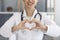 Female doctor showing heart gesture indoors. Cardiologist communicating online. Cardiac health, charity or donation
