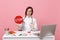 Female doctor sit at desk work on computer with medical document hold stop in hospital isolated on pastel pink wall