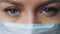 A female doctor therapist in a white robe, mask and gloves. Face close-up. The doctor cries and prays. Tears in eyes