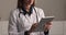 Female doctor in uniform standing alone indoor using tablet device