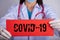 Female doctor wearing surgical mask, stethoscope and holding red torn paper with COVID-19 text. Healthcare and medical concept