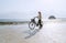 Female dressed light summer clothes have morning walk with old vintage bicycle with front basket on the lonely low tide ocean