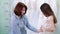 Female dressmaker looking at wedding dress on young bride in salon