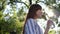 Female drinks cold mineral water from a glass bottle in backlight and smiles at sunny day