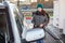 Female driver refueling car at self-service gas station, woman in coat and warm hat holding hose with nozzle and looking at camera