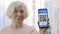 Female elderly person points into the camera a smartphone with immune digital passport for covid-19. QR Code. Crop view