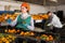 Female employee in colored uniform puts tangerines in packaging for sale