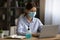 Female employee in facial mask work on laptop online