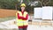 Female engineer on a construction site wearing a protective hardhat and a signal vest near the foundation of a house with formwork