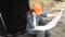 Female engineer examines a scheme sitting in a large bucket of a excavator.