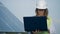 Female engineer is walking with her laptop near a solar battery