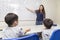 A female English teacher teaching two little boys, explaining ABC alphabet on board in classroom at school
