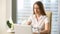 Female entrepreneur using laptop at workplace, looking at camera smiling