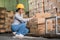 female factory worker inspecting goods while squatting holding a tablet in warehouse