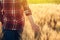 Female farmer in plaid shirt touching wheat crop ears