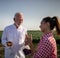 Female farmer using tablet talking with elderly scientist holding soil sample