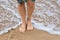 Female feet barefoot with anklet standing in waves on the surf line