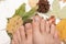 Female feet with beige nail polish. Woman legs with autumn nail design on wooden background with fallen leaves