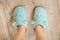 Female feet in blue cozy slippers on a wooden floor at bedroom close-up. Concepts of comfy soft fleece home shoes and warm