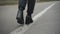 Female feet in jeans and black leather high-heels walking along white line road marking. Unrecognizable young woman