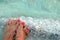 Female feet with manicure on stone, covered with salt formations between the waves in the water. Crystallization of salt on stone