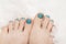 Female feet with marine nail design. Glitter cyan nail polish pedicure on white fluffy background