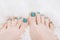 Female feet with marine nail design. Glitter cyan nail polish pedicure on white fluffy background