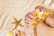 Female feet with pretty multicolor pedicure on sand, with frangipani flowers and seashells. Summertime concept