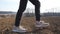 Female feet of small kid goes on the dry ground along ploughed meadow at sunny day. Legs of little girl in sneakers