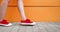 Female feet in sneakers gumshoes walking along orange wall, close up. Woman`s feet in red sports shoes walking along the