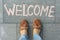 Female feet with text welcome written on grey sidewalk