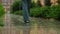 Female feet walking on the street on puddles. Woman steps by the wet road through the city under the rain. Rainy summer