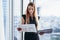 Female financial analyst holding papers studying documents standing against window with city view