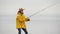 Female fisher woman in yellow raincoat throws fishing tackles with spinning rod in slow motion