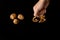 Female fist is beating shell of walnuts on the black table/background. Three walnuts are near on the black table/background. World