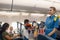 Female flight attendant serving food to passengers on aircraft. Hostess walking with trolley on aisle