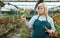 Female florist in apron with scissors working with red begonia in hothouse