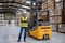 Female forklift driver standing by forklift. Warehouse worker preparing products for shipmennt, delivery, checking stock